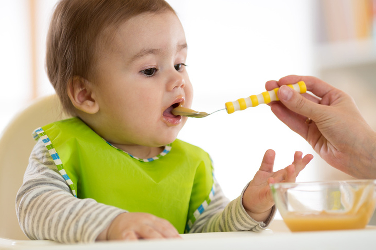 Baby eating food with mother help