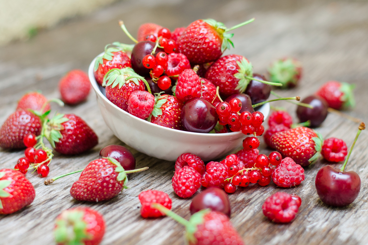 Ripe fruit and berries in a white cup on a wooden table
