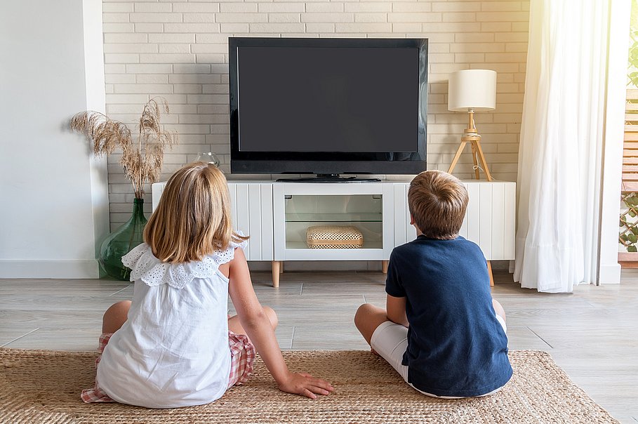 Zwei Kinder sitzen auf dem Wohnzimmerboden und sehen fern. 