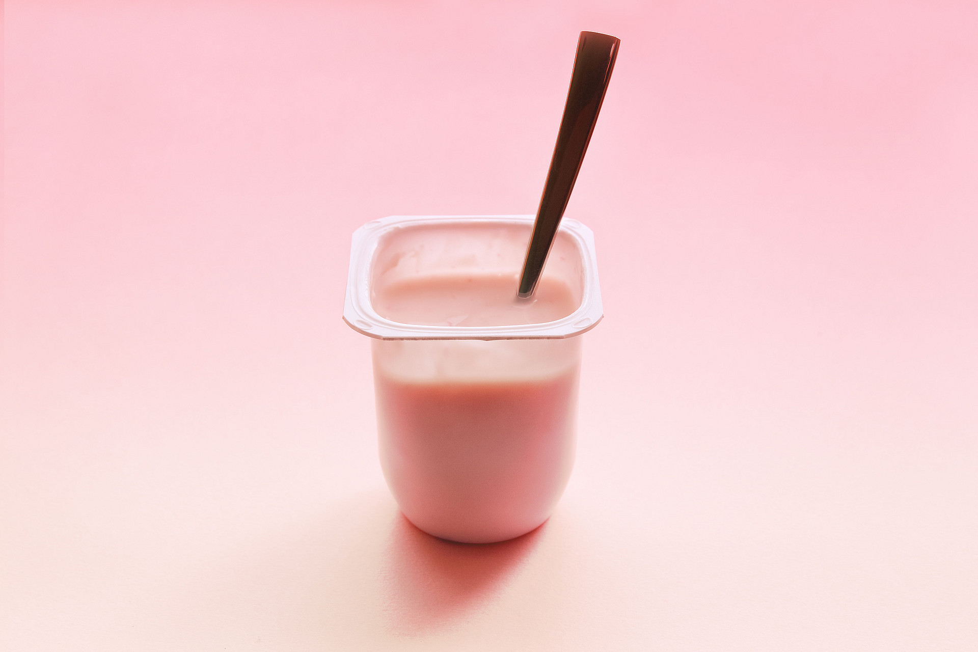 Erdbeerjoghurt in einem Plastikbecher mit einem Löffel auf einem rosafarbenen Hintergrund