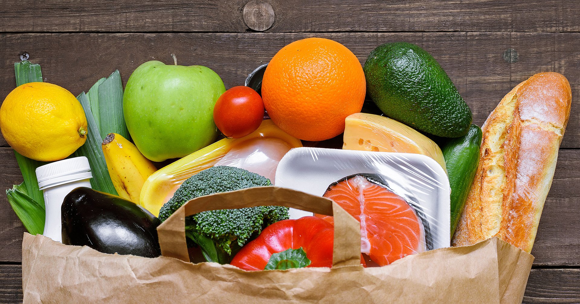 Different food in paper bag on rustic wooden background,