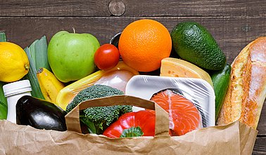 Different food in paper bag on rustic wooden background,