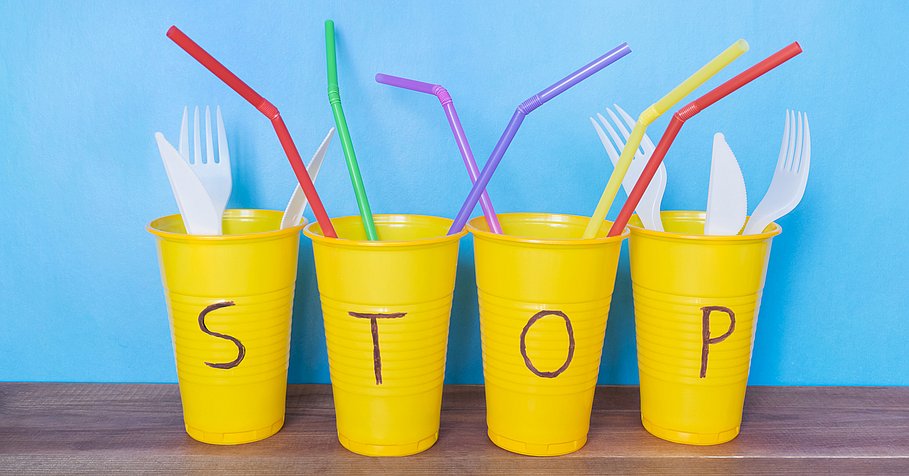 vier gelbe Plastikbecher mit Plastikbesteck und Strohhalmen