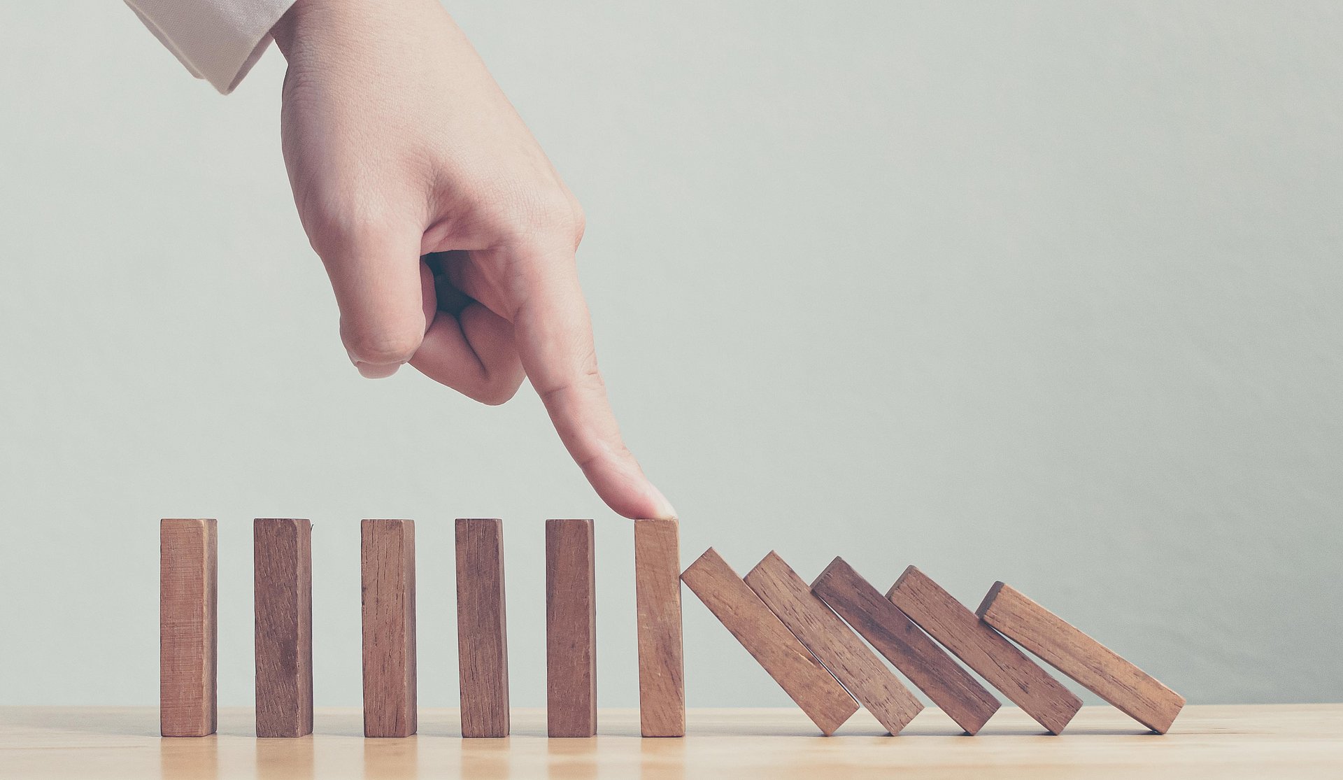 Hand stopping wooden domino business crisis effect or risk protection concept Hand stopping wooden domino business crisis effect or risk protection concept