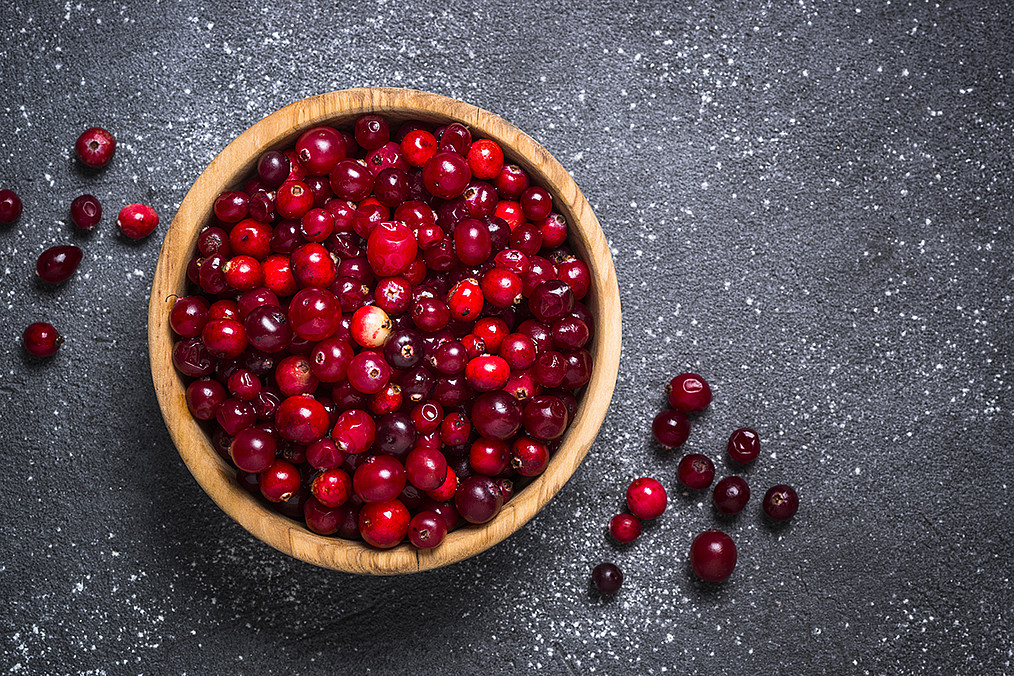 Cranberry in wooden bowl on black stone background.