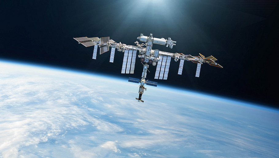 Ein Bild der ISS wie sie im Weltraum schwebt, im Hintergrund sieht man die Erde