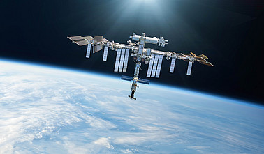 Ein Bild der ISS wie sie im Weltraum schwebt, im Hintergrund sieht man die Erde