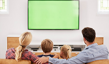 Familie mit zwei Kindern sitzen auf einem Sofa vor dem Fernseher