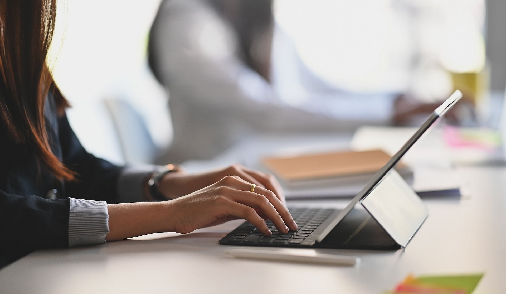 Cropped shot of business woman hand while typing on computer tablet and sitting next to her colleague.
