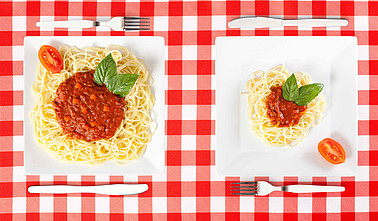 Zwei Teller mit jeweils einer großen und einer kleinen Portion Spaghetti