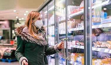 Woman at supermarket freezer section wearing face mask